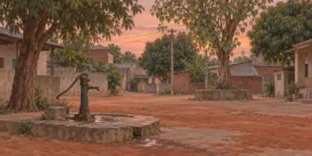 A hand pump in a village square in evening light