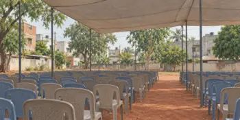 Rows of empty plastic chairs in an open ground under a canopy
