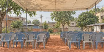 Rows of empty plastic chairs in an open ground under a canopy